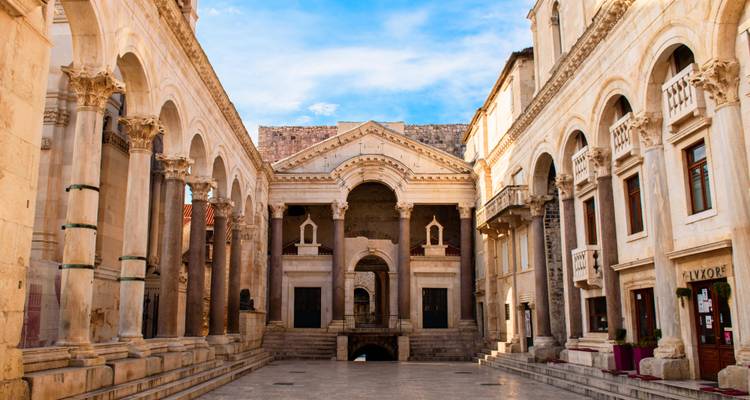 Cour à péristyle du palais de Dioclétien encadrée par des colonnes et des arches romaines sous un ciel bleu à Split.