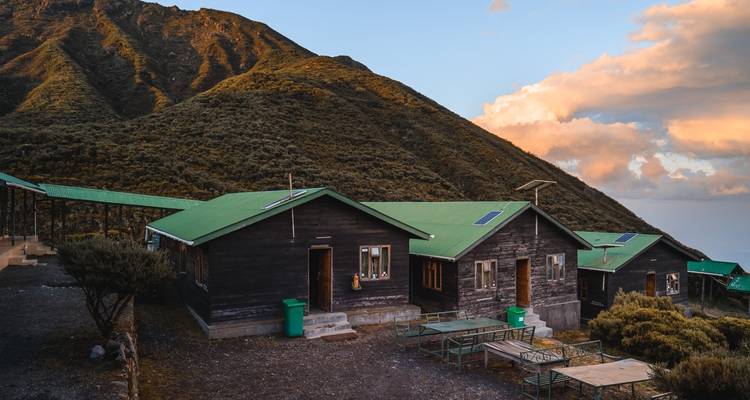 Cabaña con techo verde en un entorno montañoso al atardecer.