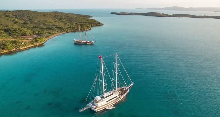 Two sailboats anchored in a tranquil turquoise bay.