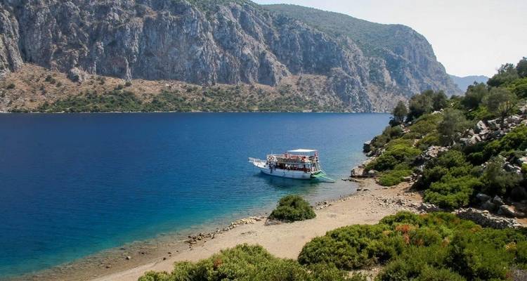 Boat on a rocky, forested shoreline by clear blue water.