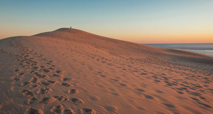 Duinlandschap met persoon bovenop tijdens zonsondergang