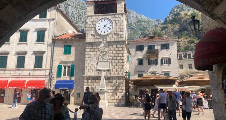 Tour d'horloge sur une place publique, entourée de gens et de cafés.