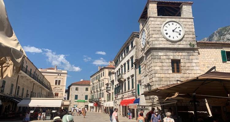 Bâtiment en pierre avec une tour d'horloge sur une place animée.