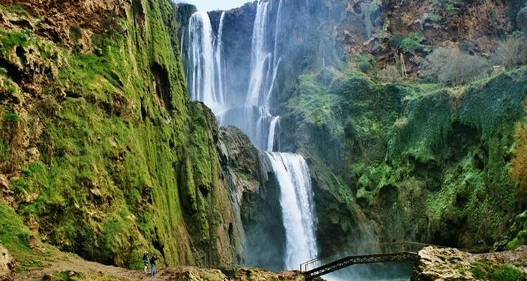 Mensen in de buurt van een grote waterval met weelderige groene omgeving.