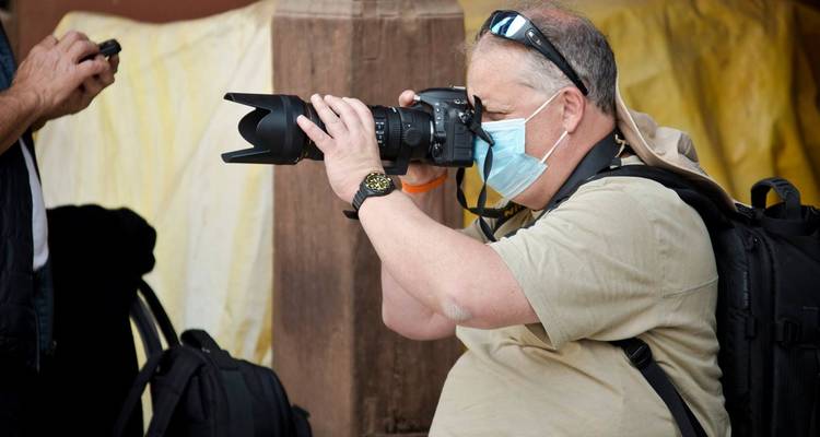 Une personne portant un masque utilisant un appareil photo professionnel, avec des sacs à dos autour.