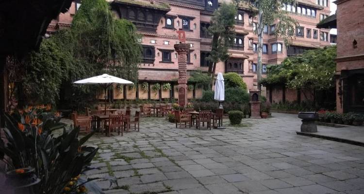 Une cour paisible dans un jardin avec des tables et des parasols, entourée de bâtiments de style ancien.