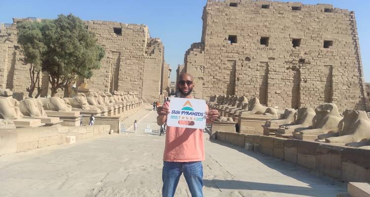 Persoon die voor tempelruïnes met een bord staat.