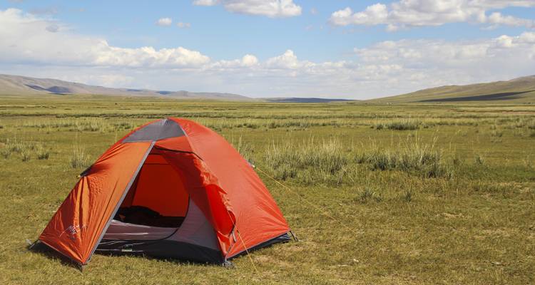 Une tente de camping installée sur des prairies luxuriantes avec des collines au loin.
