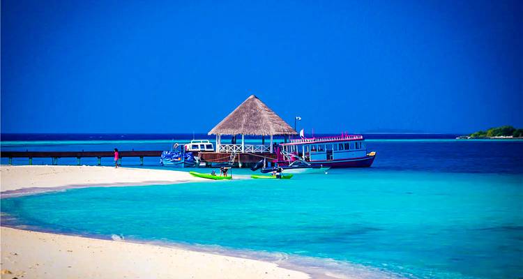Océan turquoise avec une jetée, des bateaux et des gens sur une plage tropicale.