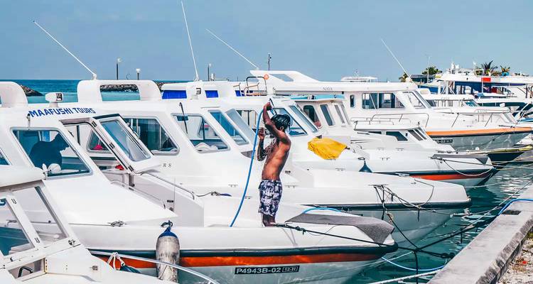 Homme nettoyant un bateau dans une marina sous un ciel nuageux.