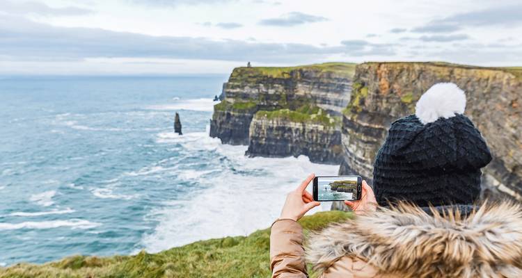 Falaises de Moher vues avec une personne prenant une photo depuis le bord.