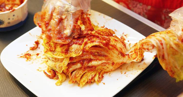 Manos enguantadas mezclando pasta de pimienta roja picante en col napa mientras se prepara kimchi.