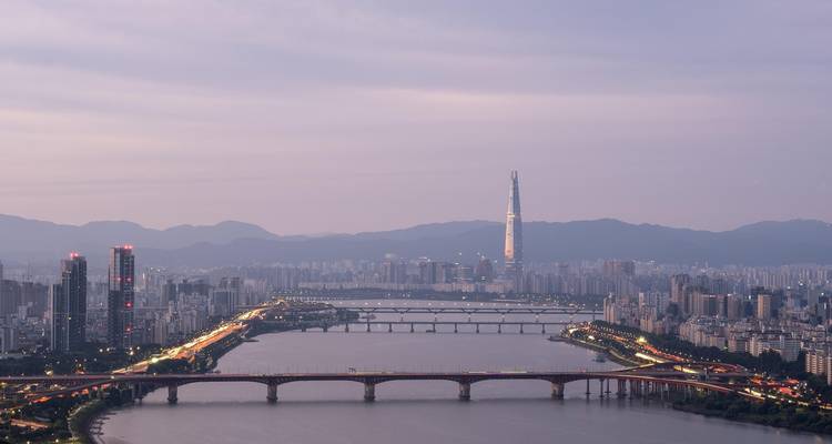 Twilight aerial view over Seoul’s Han River with multiple bridges and the Lotte World Tower on the horizon.