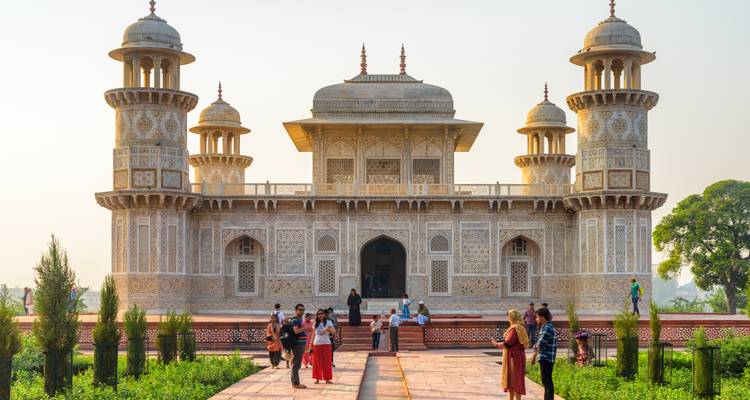 Los visitantes explorando la intrincada fachada de mármol de la Tumba de Itimad-ud-Daulah bajo la suave luz del atardecer