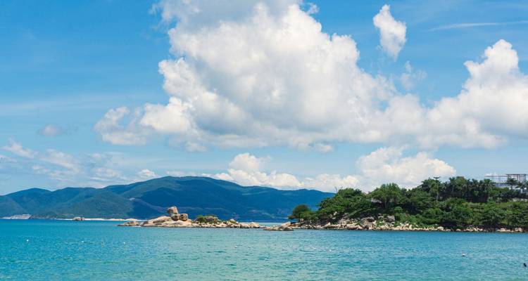 Pequeña isla cubierta de árboles y mar turquesa bajo nubes blancas ondeantes.