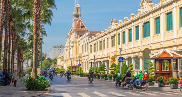 Bulevar colonial lleno de vida, con árboles altos, edificios clásicos y motos por todos lados.