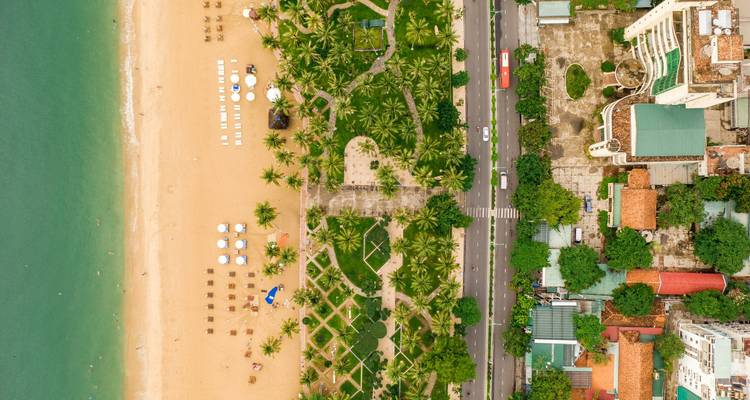 Vista aérea con dron mostrando el contraste entre las calles de la ciudad, jardines con palmeras y playa de arena.