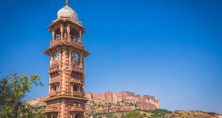 Uhrenturm mit einer Festung im Hintergrund unter einem klaren blauen Himmel.