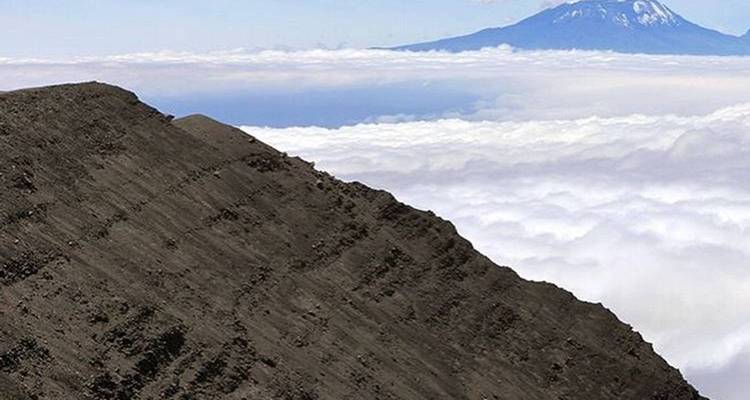 Pente d'une montagne avec un sommet distant visible au-dessus des nuages.