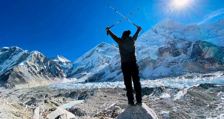 Persoon die triomfantelijk poseert met trekkingstokken voor besneeuwde bergtoppen.