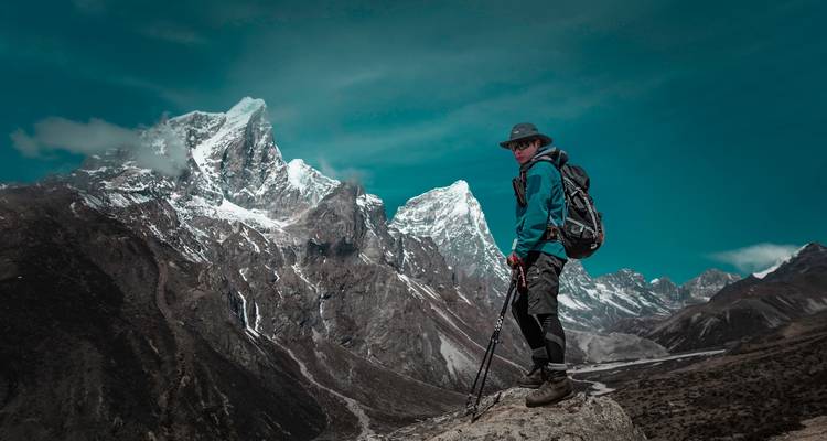 Wandelaar met trekkinguitrusting poserend op rotsachtig terrein met dramatische bergachtergrond.