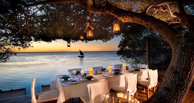 Outdoor dining setup by the water at sunset.