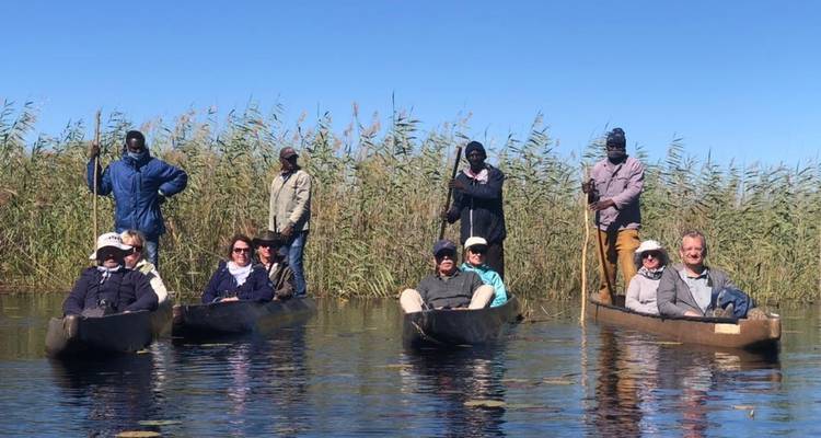 People sitting in canoes on a calm water body with reeds.