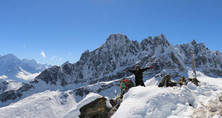 Personne debout sur une montagne enneigée avec des pics rocheux en arrière-plan.