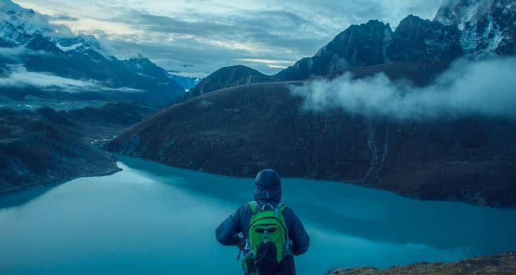 Personne avec un sac à dos regardant au-delà d'un lac avec des montagnes au loin.