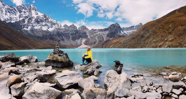 Personne assise au bord d'un lac rocheux avec des montagnes en arrière-plan.