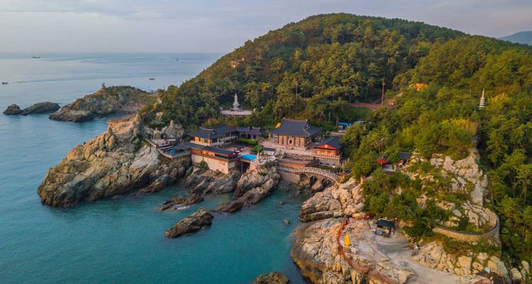 Vue aérienne d'un complexe de temple bouddhiste en falaise surplombant la mer turquoise et le cap boisé