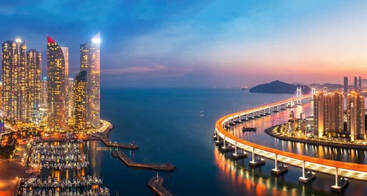 Vue panoramique au crépuscule des gratte-ciel de Busan, de la marina et du pont suspendu incurvé illuminé