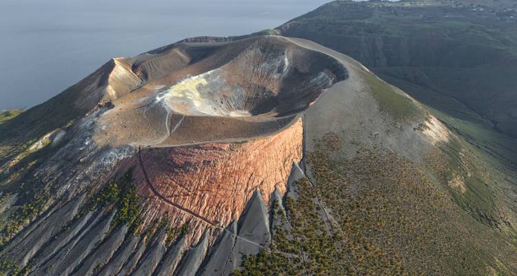 Cratère volcanique avec roches sombres et terrain environnant.