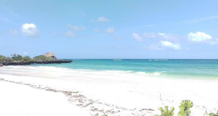 Wit zandstrand met turquoise water en verre rotsen.