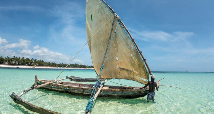 Man die naast een traditionele boot in helder ondiep water staat.