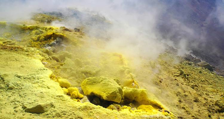 Dépôts de soufre jaune avec vapeur sur une surface volcanique.