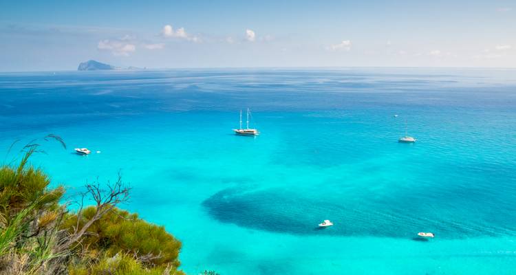Vaste océan turquoise avec voiliers et île au loin.