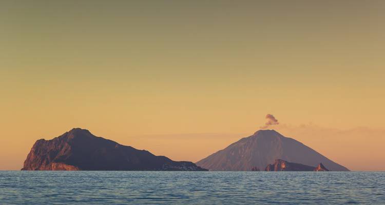 Îles volcaniques avec un sommet fumant au coucher du soleil.