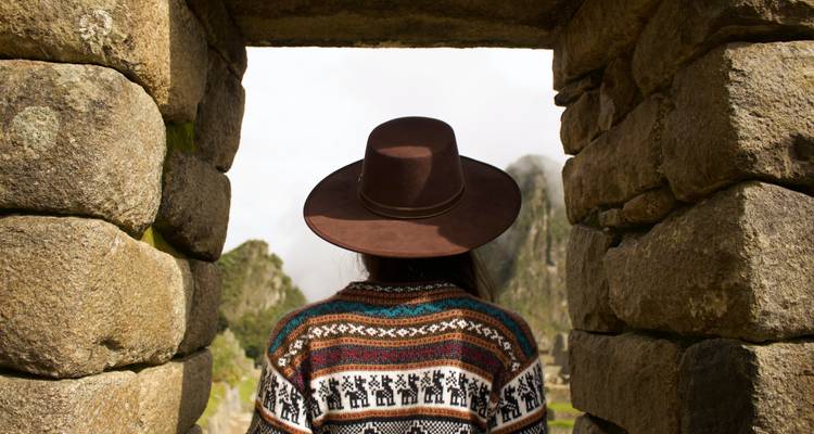 Person in traditioneller Kleidung, die durch einen alten steinernen Türbogen blickt.