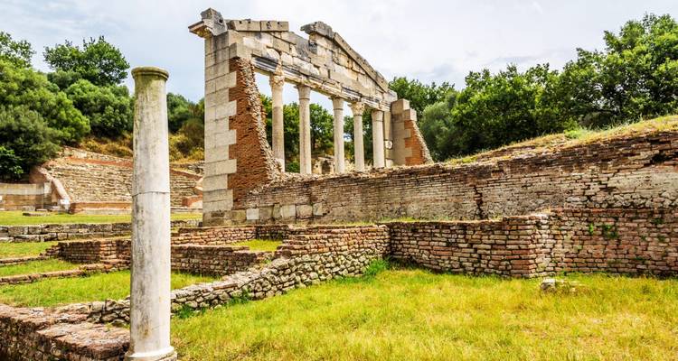 Oude ruïnes van stenen zuilen en boogconstructies in een veld.