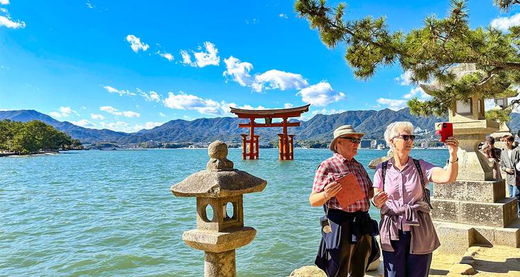 Turistas tomándose selfies cerca de una famosa puerta torii en un entorno pintoresco.