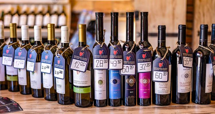 Rijen wijnflessen met prijskaartjes op een plank.