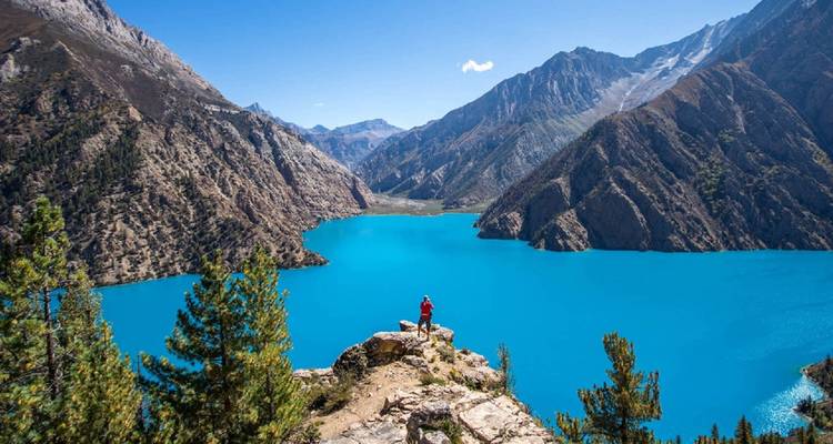 Persoon die op een klif staat en uitkijkt over een blauw meer.
