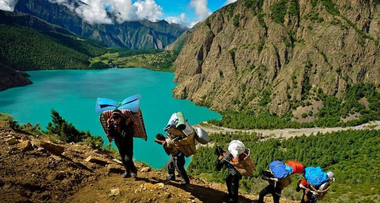 Groep wandelaars die bagage dragen op een heuvel bij een meer.