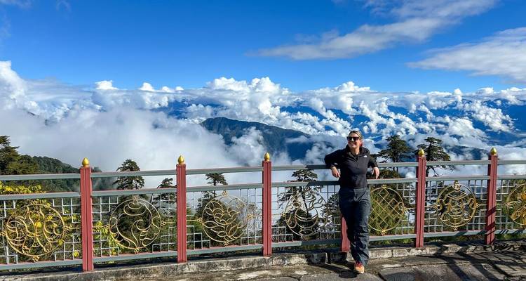 Un viajero posa en la terraza de un mirador en la montaña sobre un mar de nubes y lejanos picos del Himalaya.