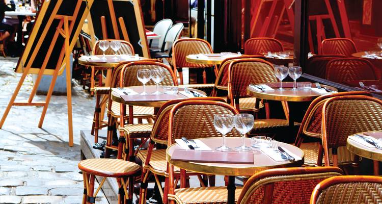 Ruelle pavée de pierres charmante bordée de tables de bistrot parisien classiques et de chaises en rotin prêtes à accueillir les clients.