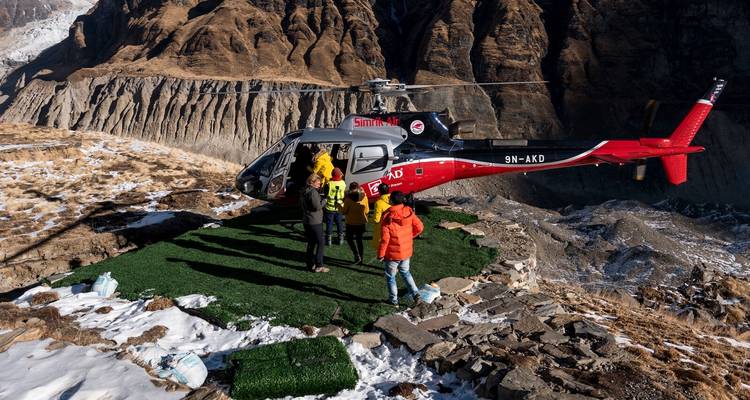 People exiting a helicopter on a grassy helipad.
