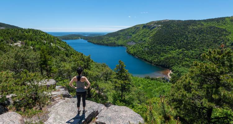 Person standing on a rock overlooking a green valley and lake.