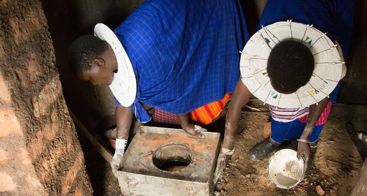 Mujeres Maasai instalando una estufa dentro de una casa de tierra tradicional.