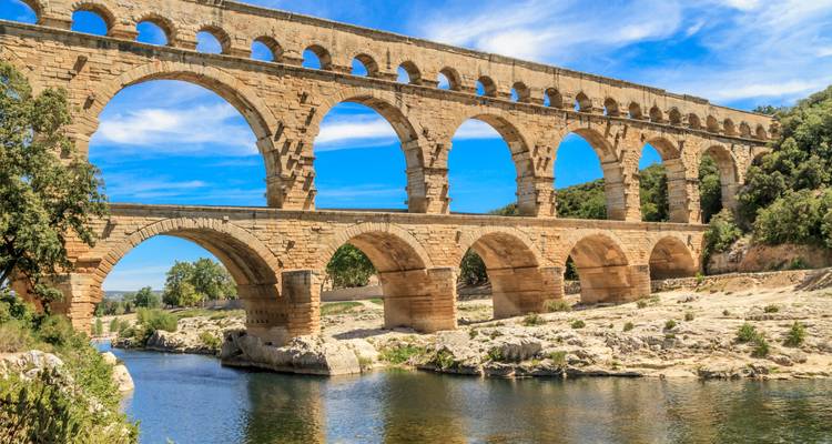Vista cercana del acueducto romano Pont du Gard que atraviesa un cañón rocoso del río bajo un cielo despejado.
